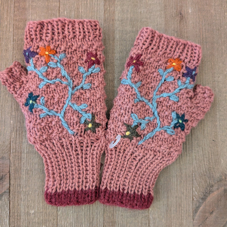 Pair of pink knitted mittens with floral patterns on a wooden surface