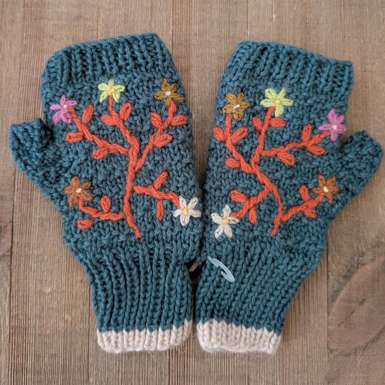 Pair of blue knitted mittens with floral patterns on a wooden surface