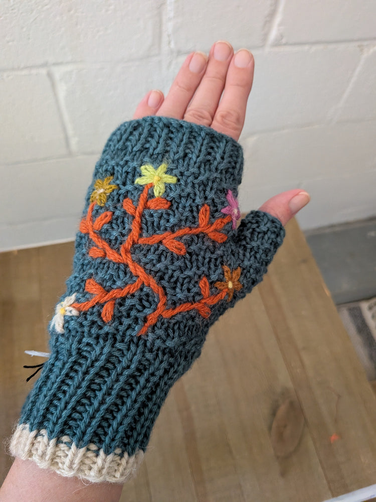 Knitted fingerless glove with floral design held against a tiled wall background
