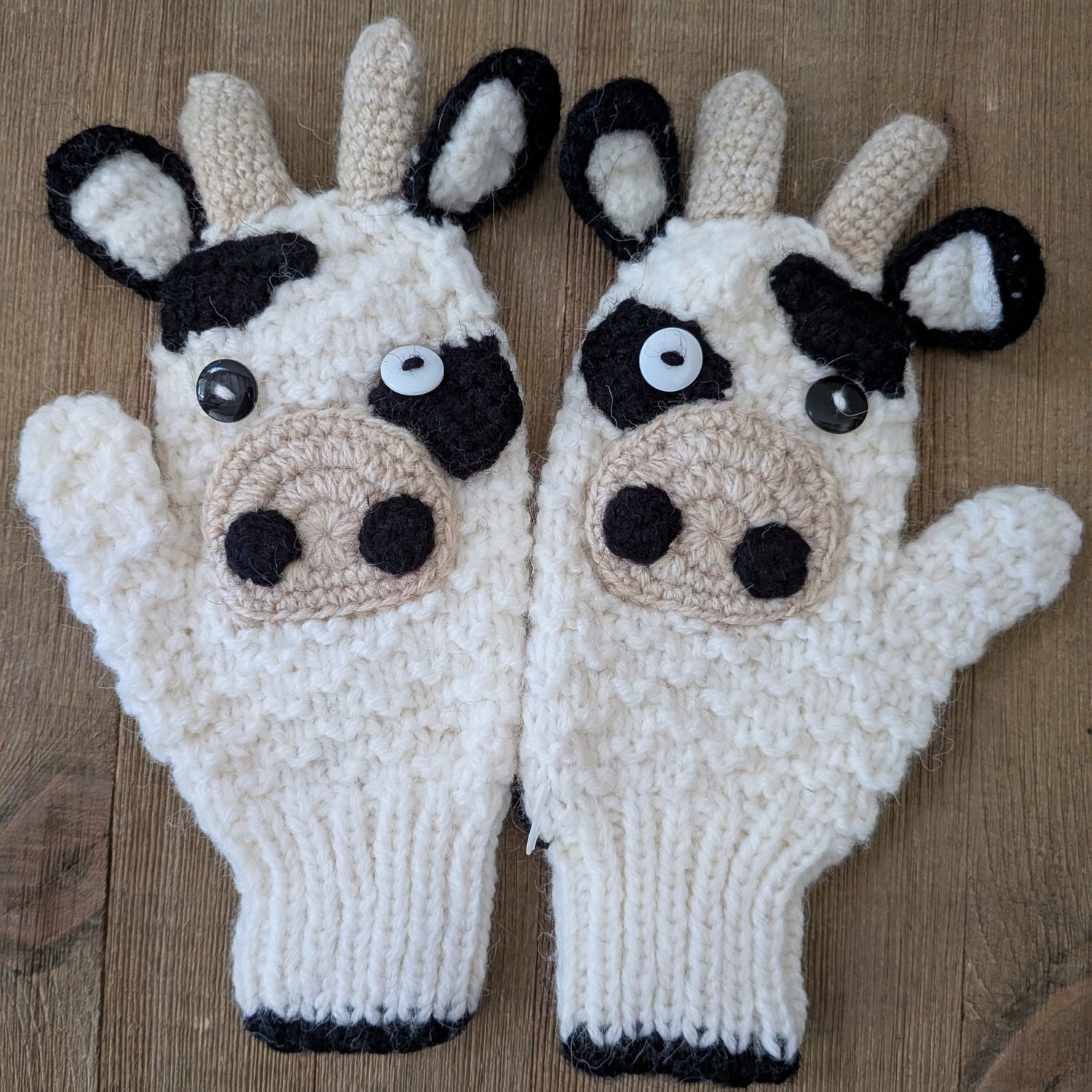A pair of kids knitted cow-themed gloves on a wooden surface