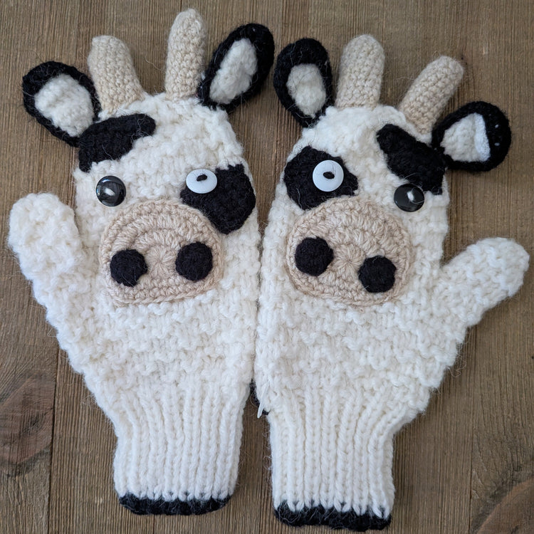 A pair of kids knitted cow-themed gloves on a wooden surface