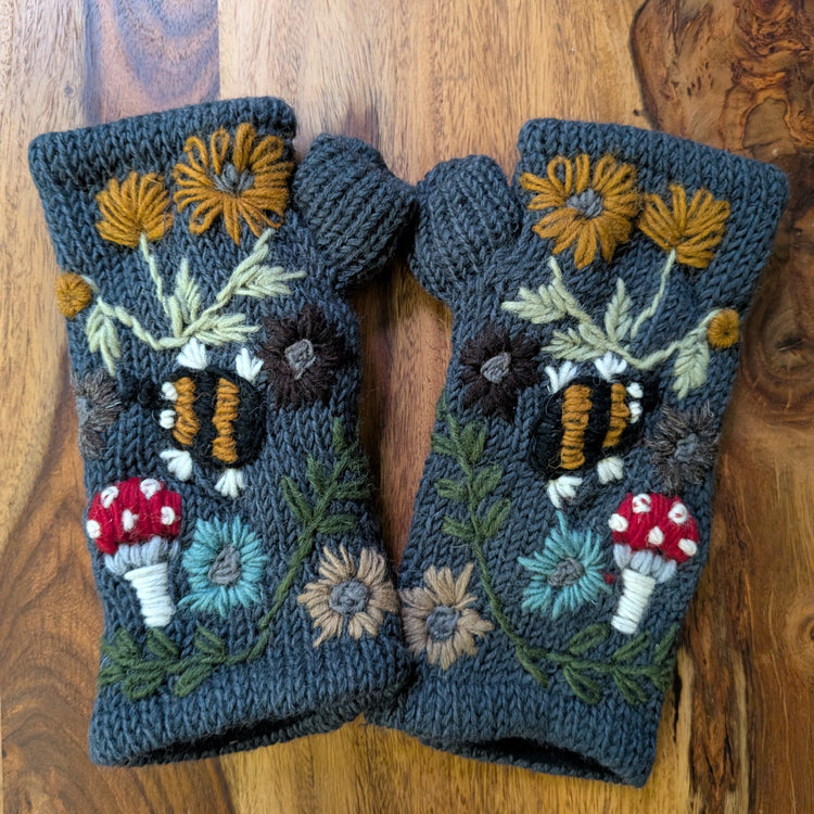 Pair of blue knitted fingerless gloves with floral and mushroom designs on a wooden surface