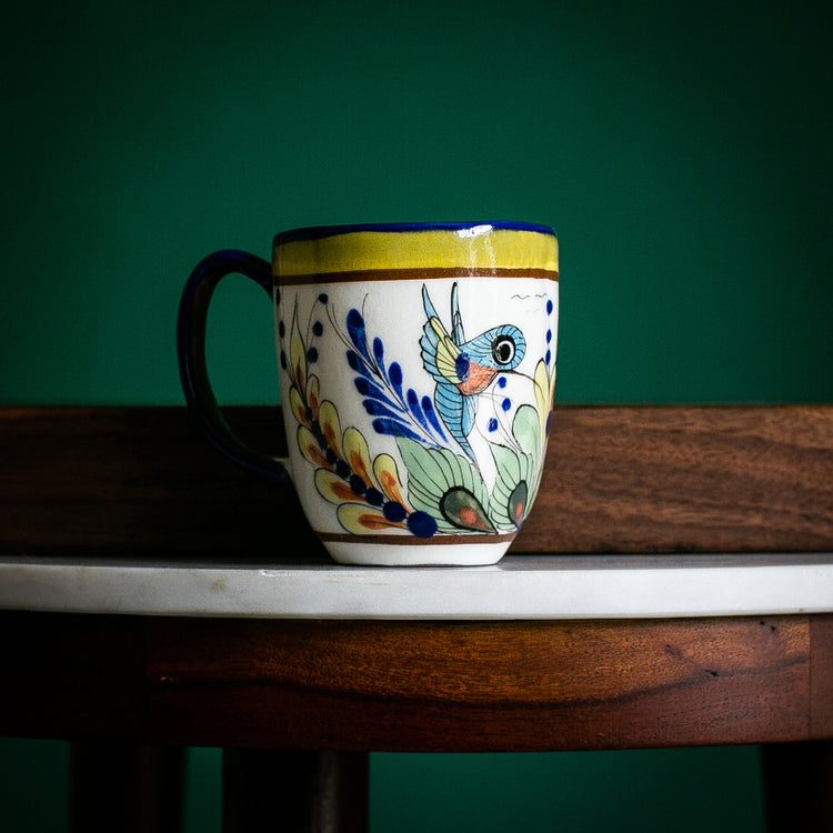A hand-painted ceramic latte cup with a wild bird pattern, featuring green, blue, and brown colors, displayed on a wooden surface with a green background.