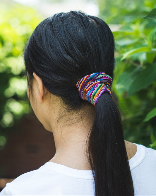 Person with a colorful Guatemalan scrunchie in a ponytail against a green leafy background