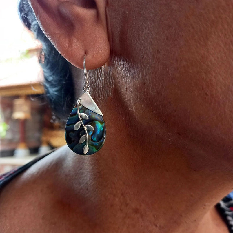 A close up of a woman wearing a teardrop-shaped Abalone earring with sterling silver leaf designs 