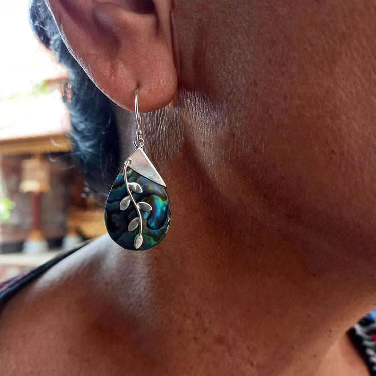 A close up of a woman wearing a teardrop-shaped Abalone earring with sterling silver leaf designs 