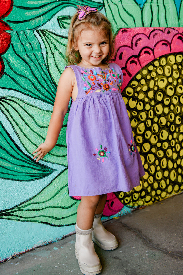 Young girl in a purple dress standing in front of a colorful floral mural.