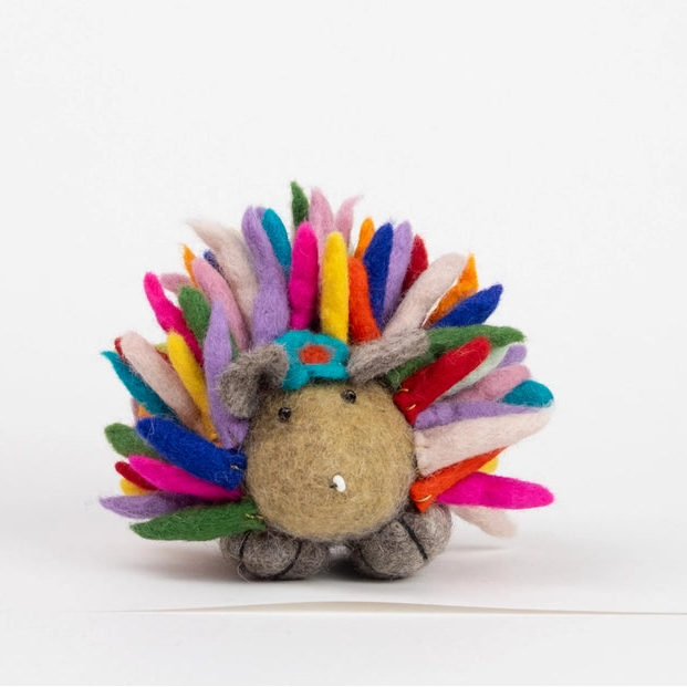 A small felt hedgehog toy with a tan face and body, gray feet, and a colorful spiky back made of felt spikes in pink, blue, yellow, orange, green, purple, and red, photographed on a clean white background.