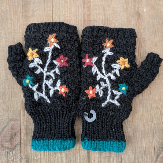 Black knitted fingerless gloves with floral patterns on a wooden surface