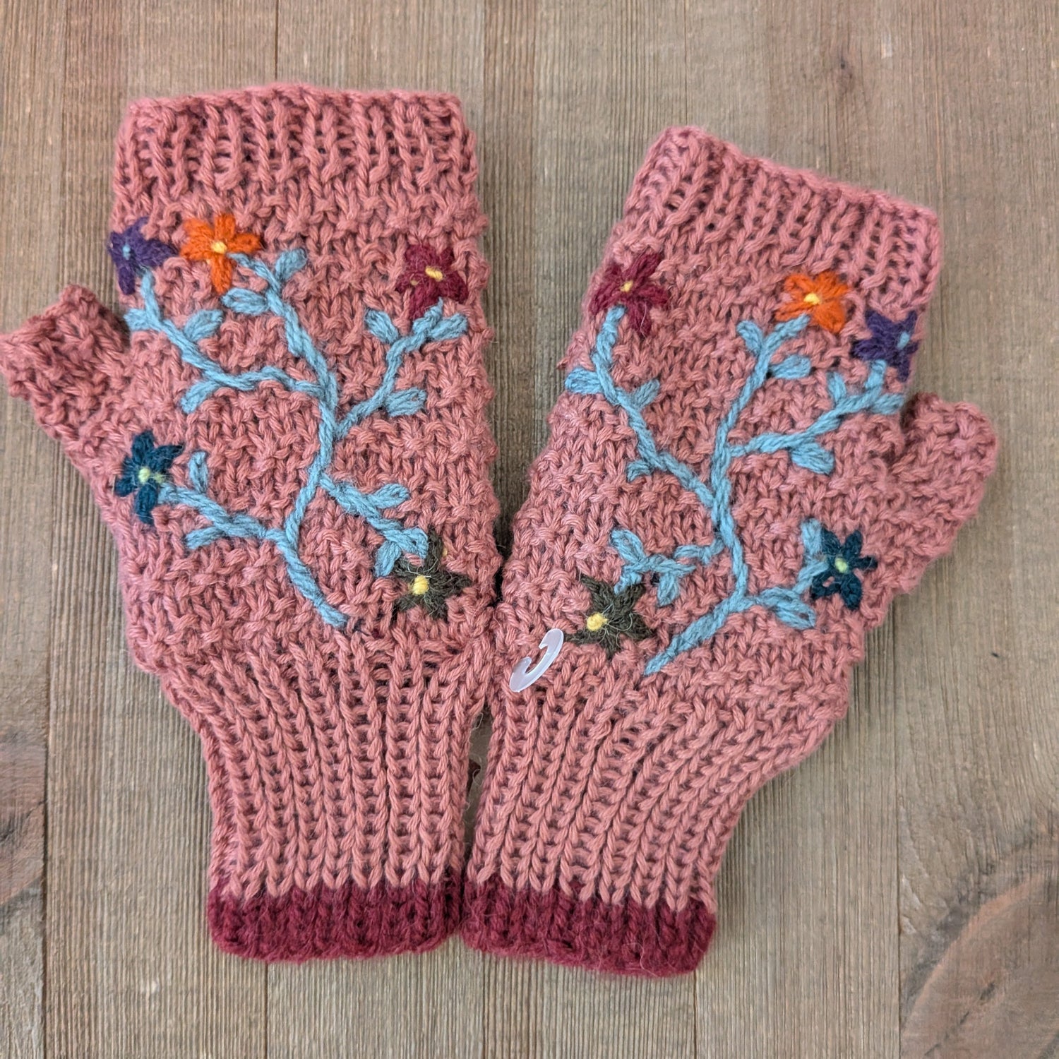Pair of pink knitted mittens with floral patterns on a wooden surface