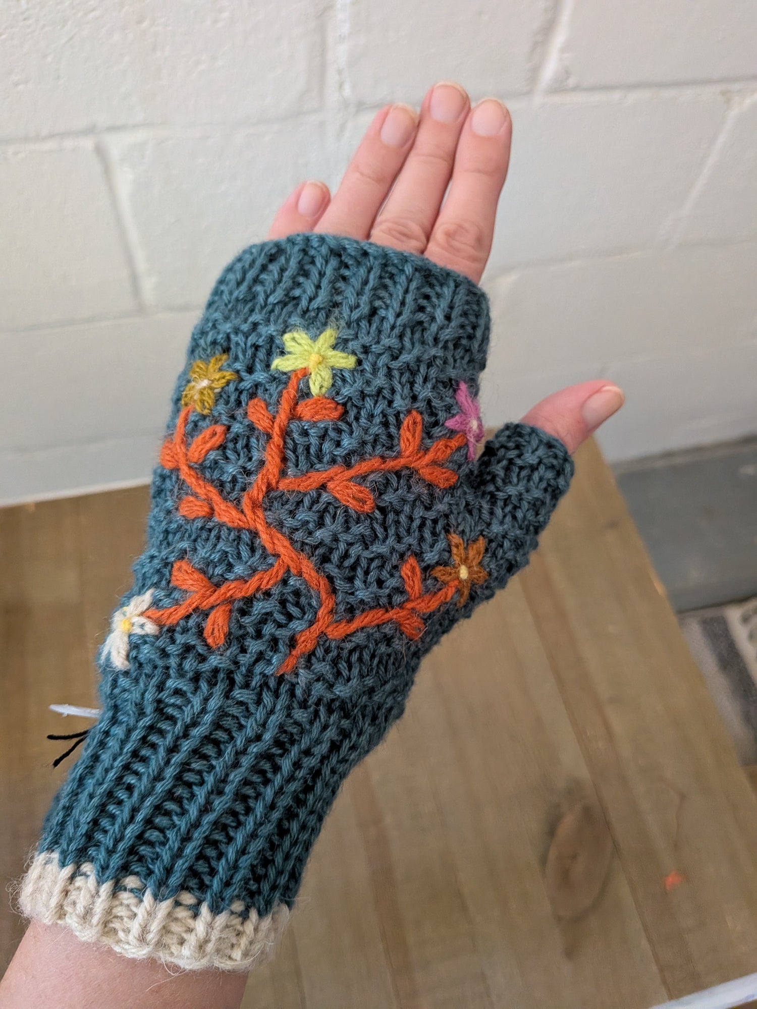 Knitted fingerless glove with floral design held against a tiled wall background