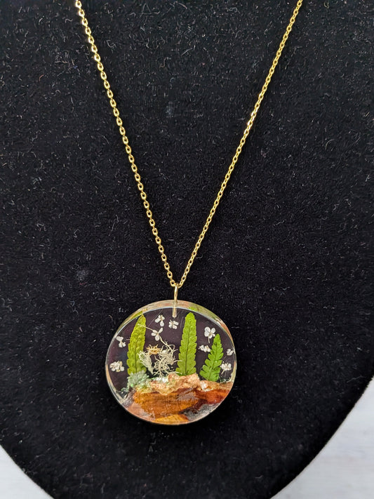 Round pendant necklace with nature-themed design on a black stand