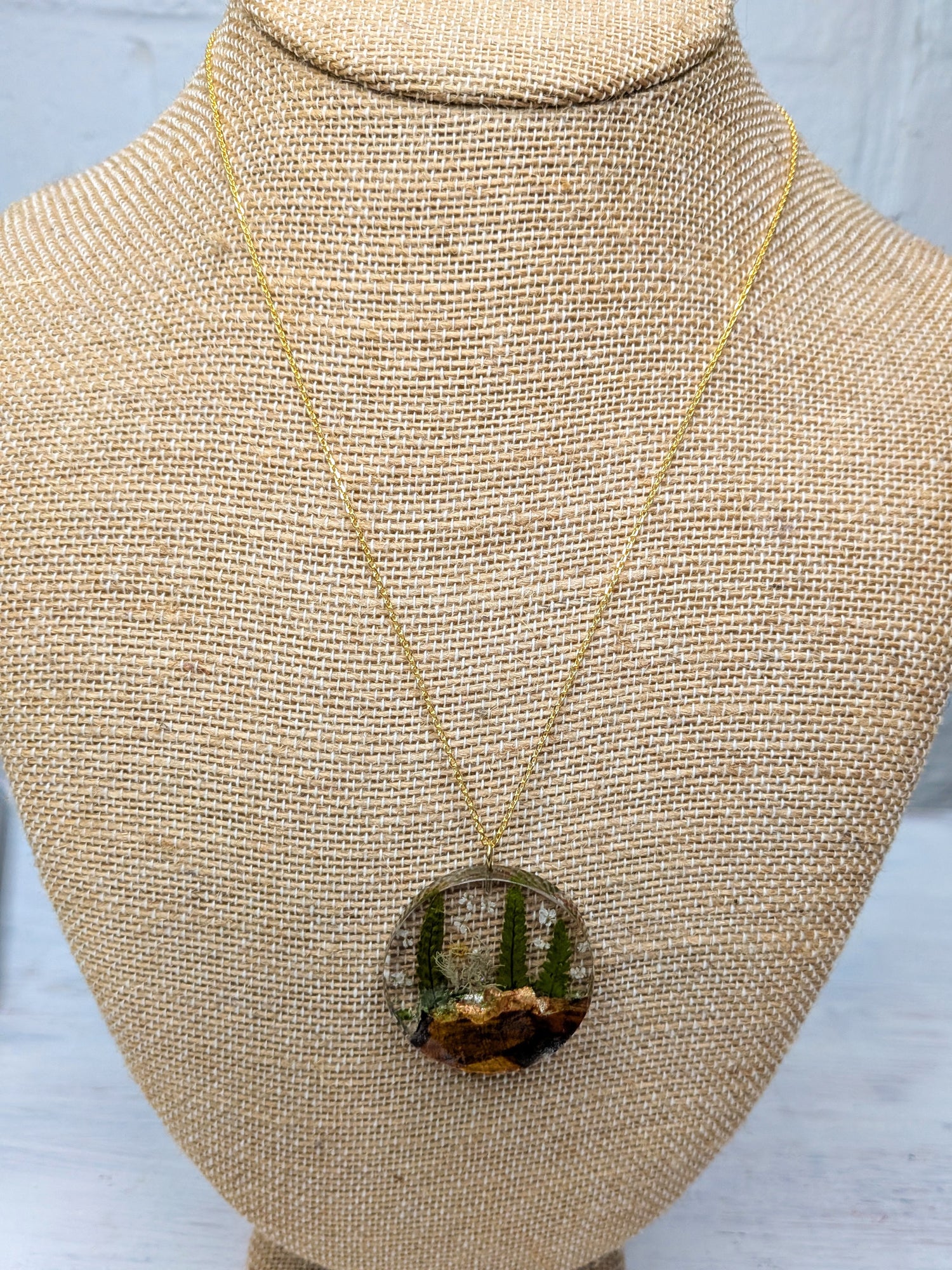 Necklace with a round nature-themed pendant featuring ferns and wood