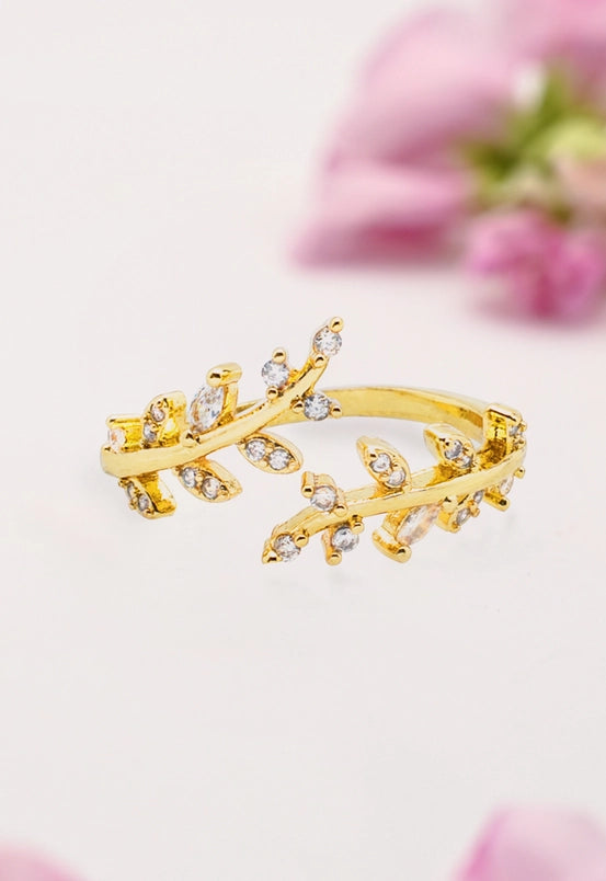 Gold ring with winding leaf shapes featuring diamond-like stones on a light background