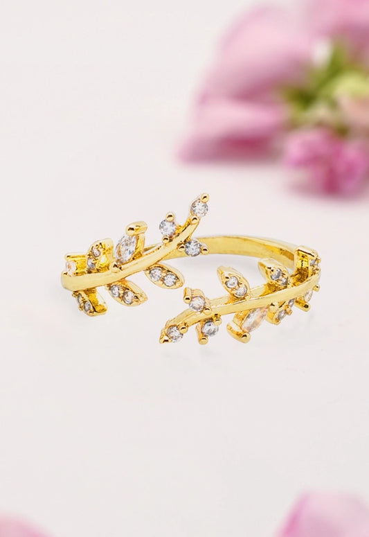 Gold ring with winding leaf shapes featuring diamond-like stones on a light background