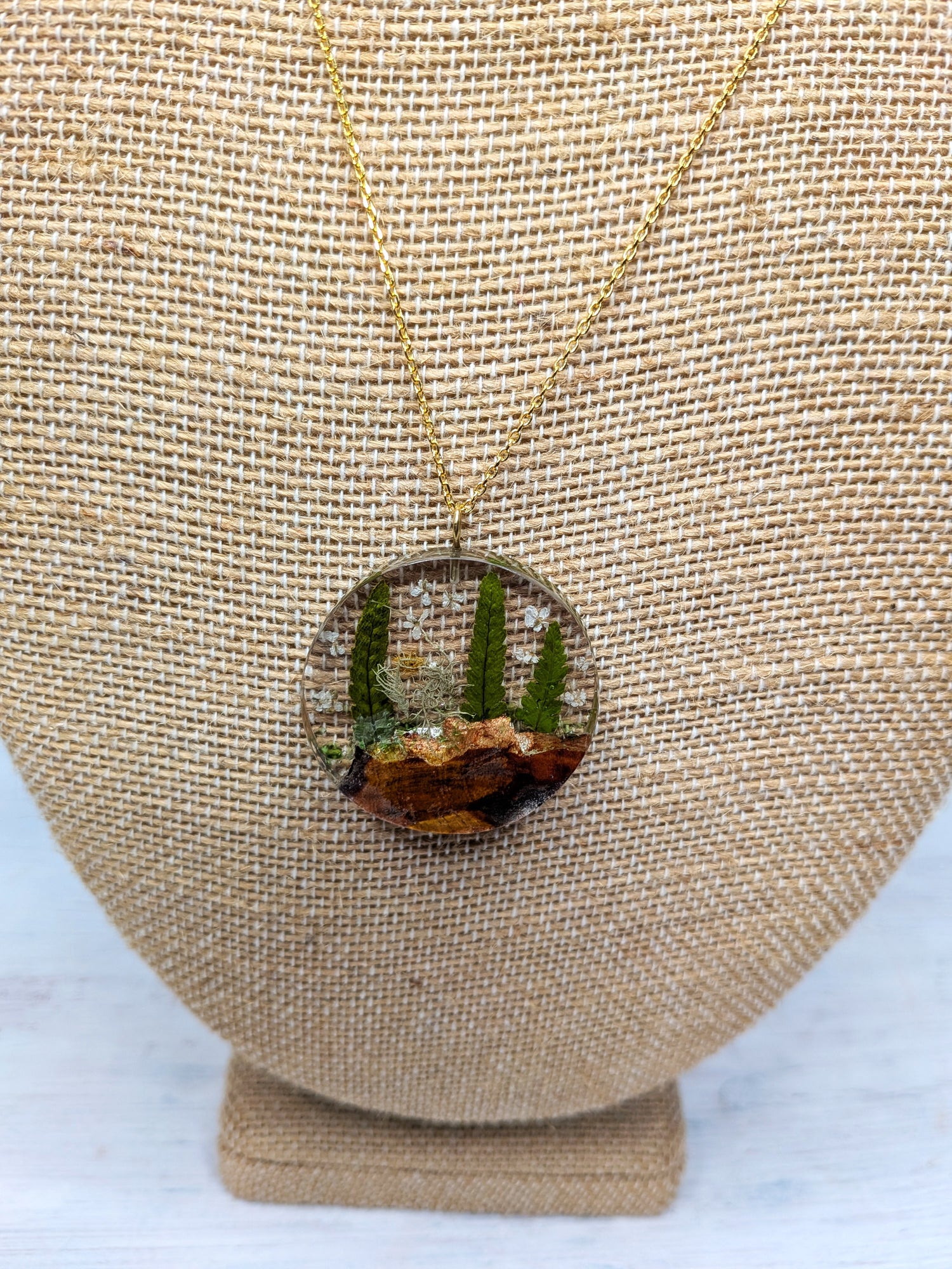 Necklace with a round nature-themed pendant featuring ferns and wood