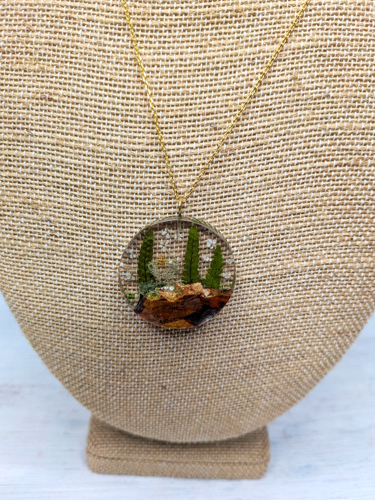 Necklace with a round nature-themed pendant featuring ferns and wood