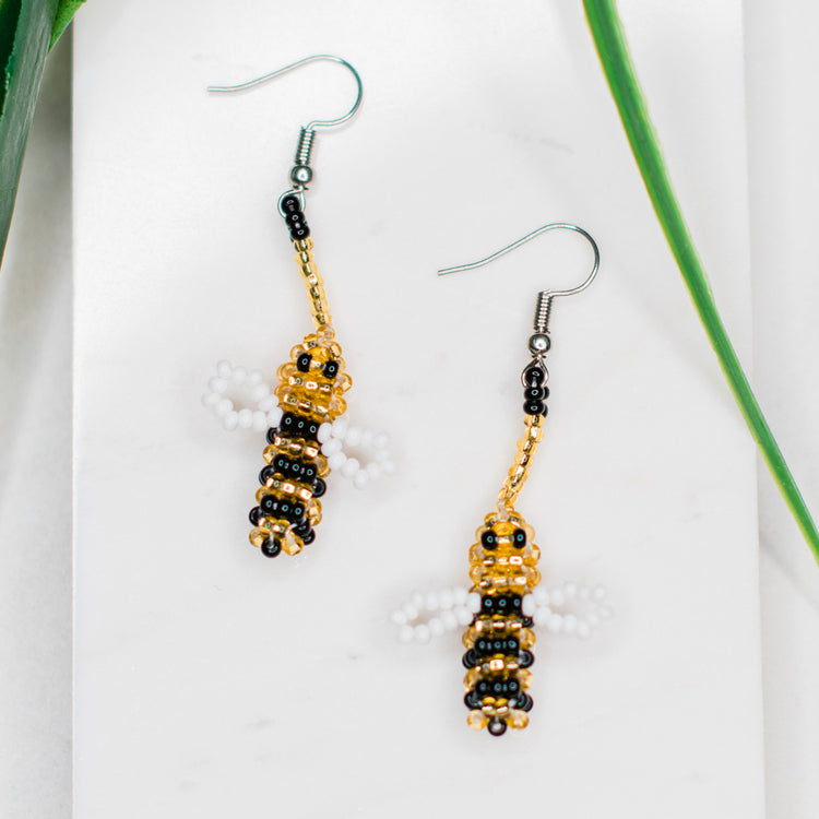 Pair of bee-shaped beaded earrings on a white background with green leaves.
