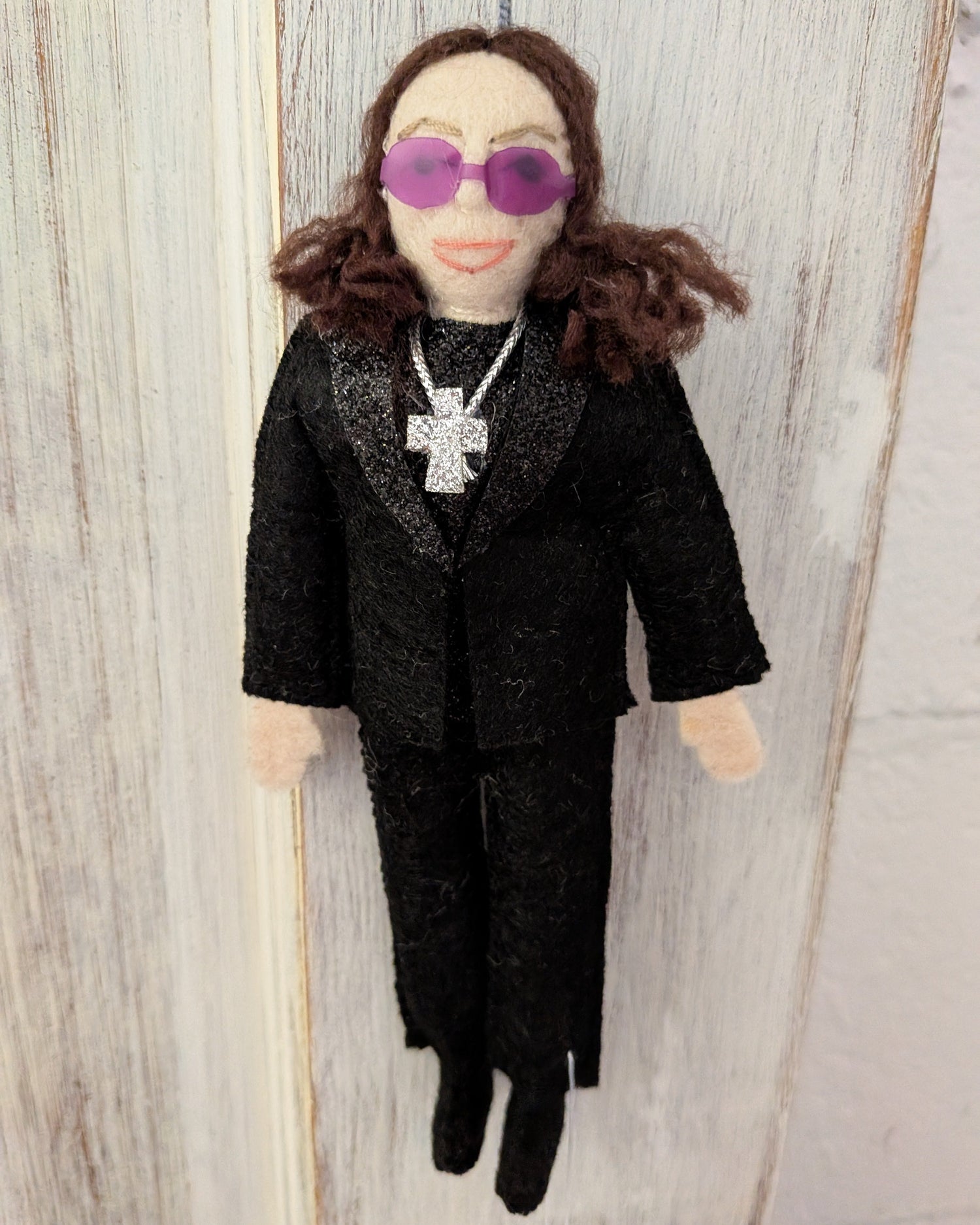 Felt Ozzy Osbourne doll wearing a black outfit with sunglasses and a cross necklace
