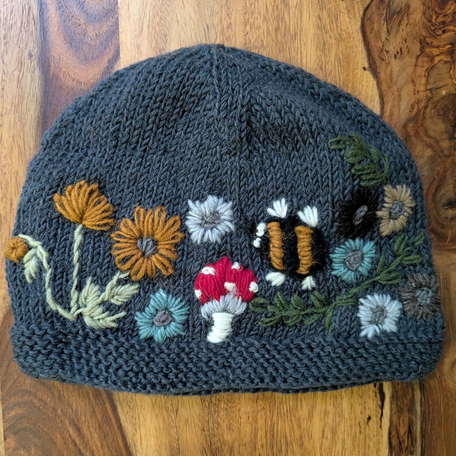 Knitted hat with floral, mushroom, and bumblebee embroidery on a wooden surface