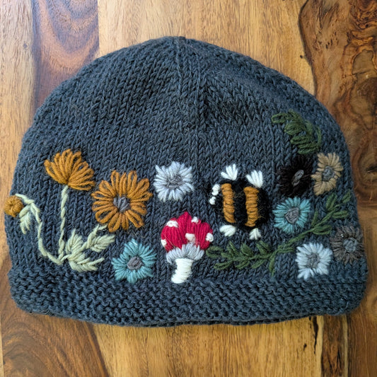 Knitted hat with floral, mushroom, and bumblebee embroidery on a wooden surface