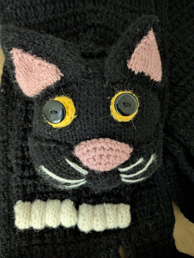 Black cat-shaped knitted scarf with pink ears and buttons on a dark background