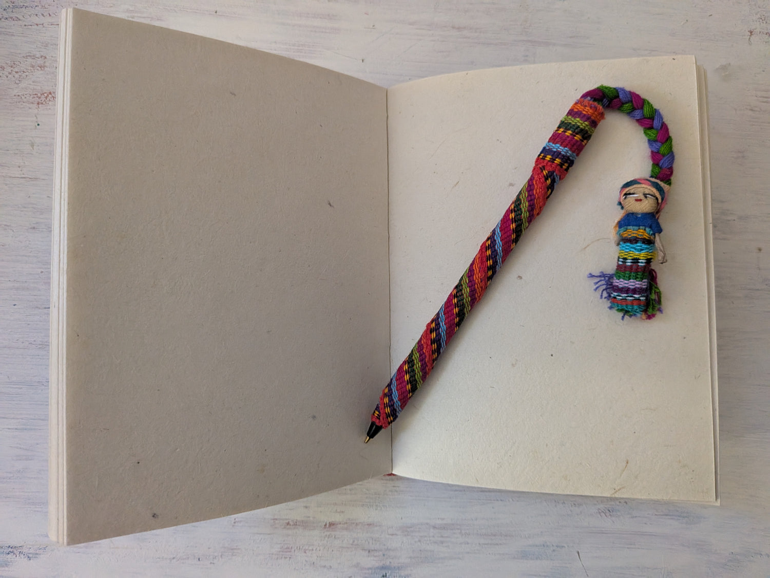 Colorful knitted bookmark with a worry doll attached on an open book with a wooden surface background