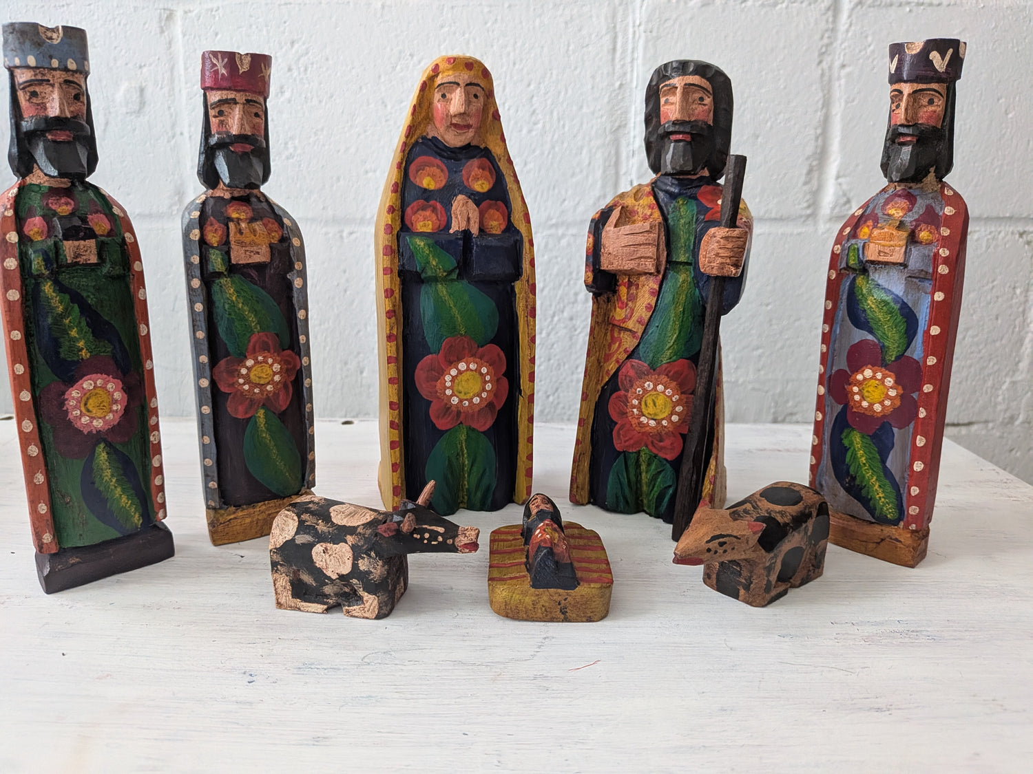 Set of hand-painted nativity scene figures on a white surface with a white brick wall background.