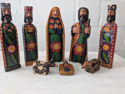 Set of hand-painted nativity scene figures on a white surface with a white brick wall background.
