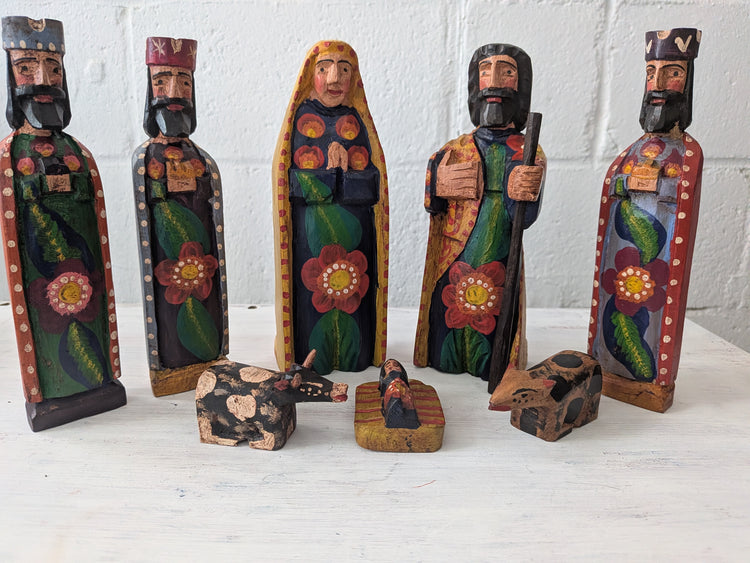 Set of hand-painted nativity scene figures on a white surface with a white brick wall background.