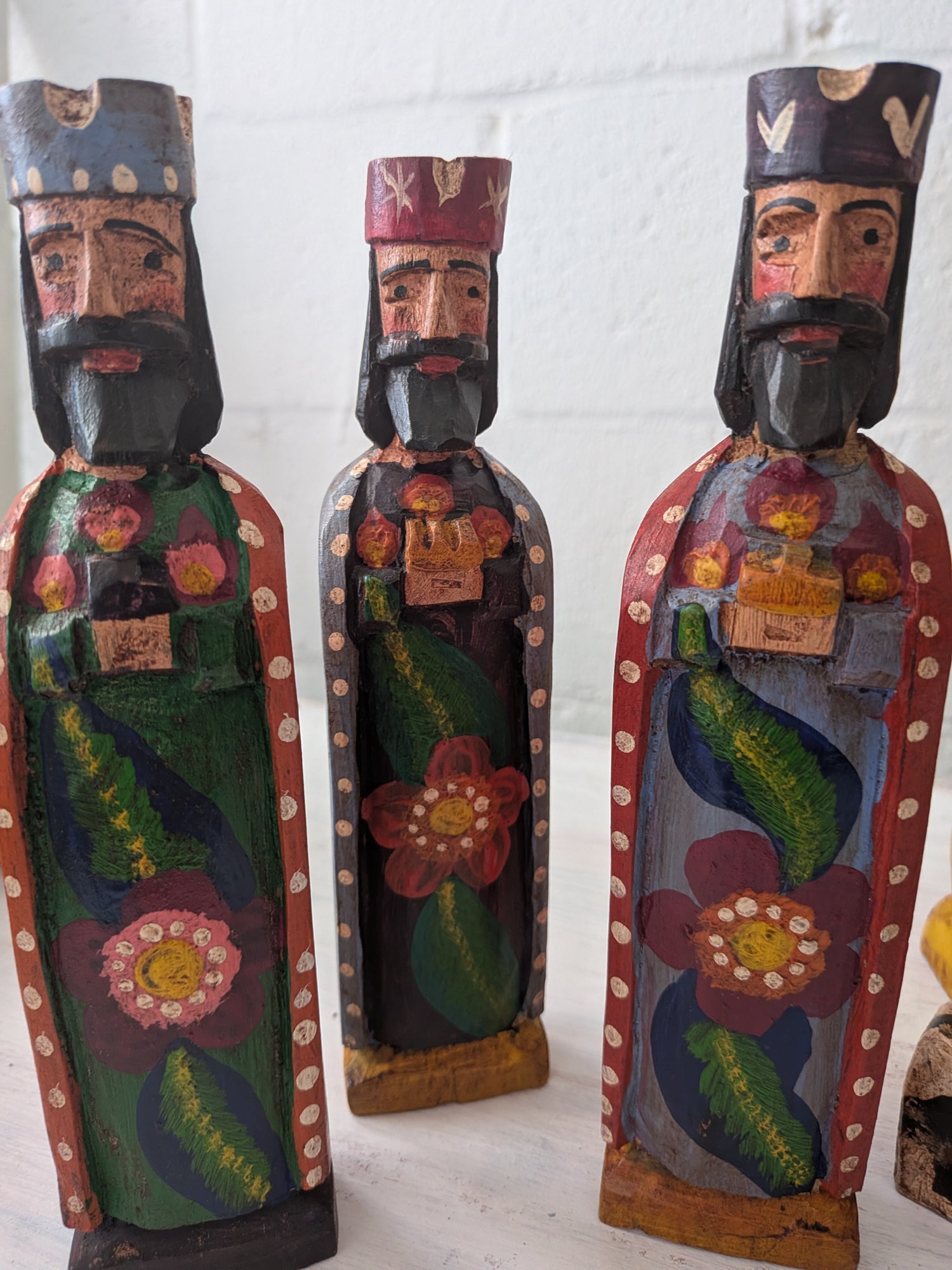 Three colorful wooden nativity figures with floral designs on a white background
