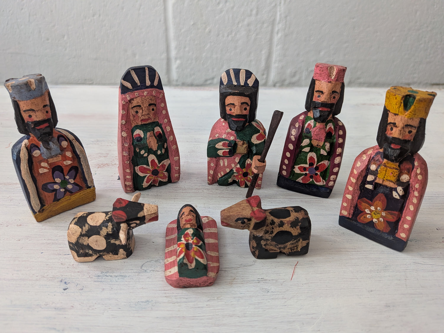 Set of hand-painted wooden nativity figures on a white surface with a light gray background.