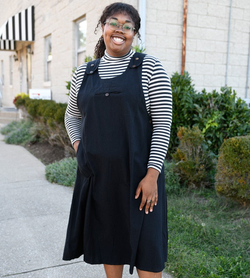 Person wearing a black jumper dress with a striped shirt outdoors.
