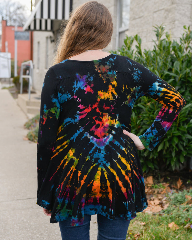 Person wearing a tie-dye shirt with colorful patterns outdoors.