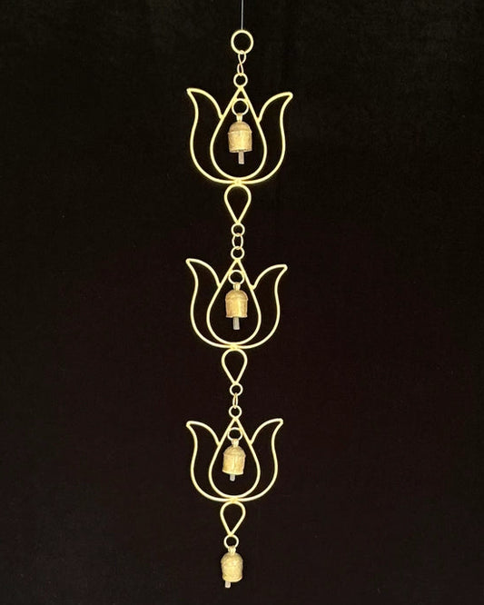 A gold-toned metal wind chime featuring three lotus-shaped ornaments with hanging bells, suspended against a solid black background.