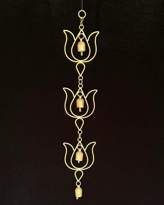A gold-toned metal wind chime featuring three lotus-shaped ornaments with hanging bells, suspended against a solid black background.