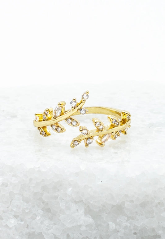A gold-colored adjustable ring with a willow branch design, adorned with small zircon stones, displayed on a marble surface.
