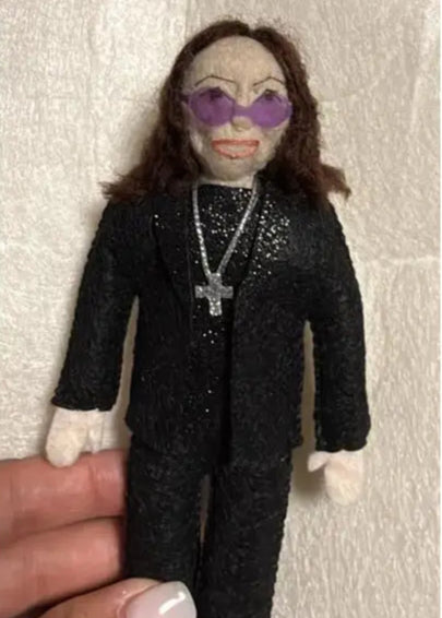 Felt Ozzy Osbourne doll wearing a black outfit with sunglasses and a cross necklace