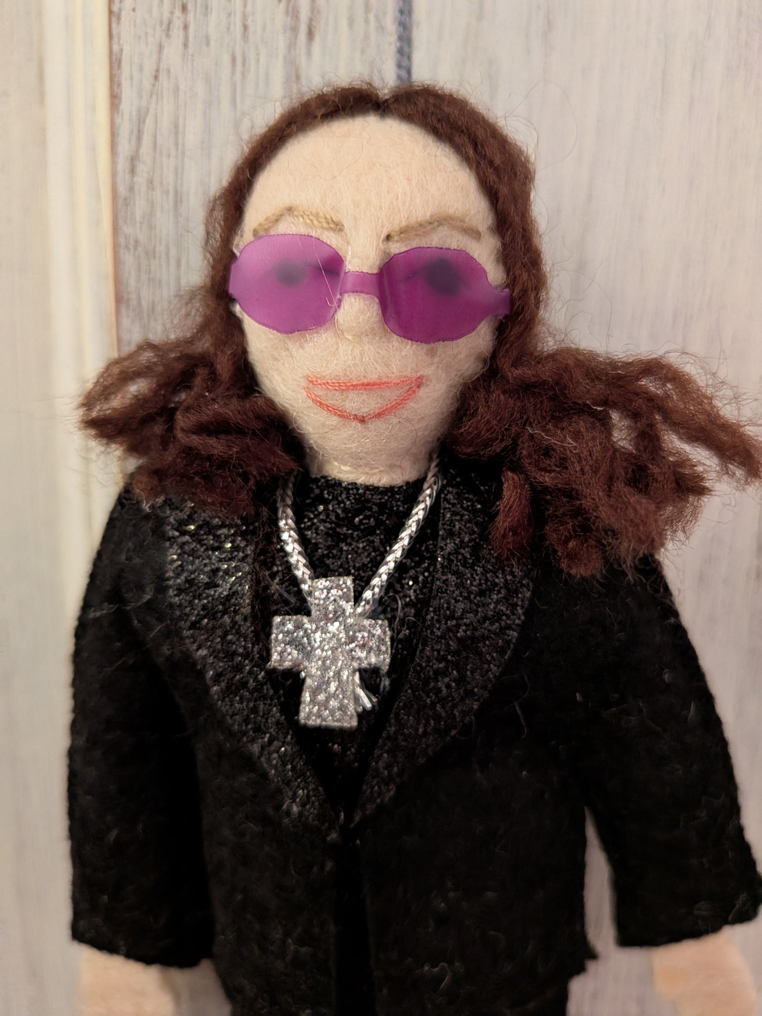 Felt Ozzy Osbourne doll wearing a black outfit with sunglasses and a cross necklace