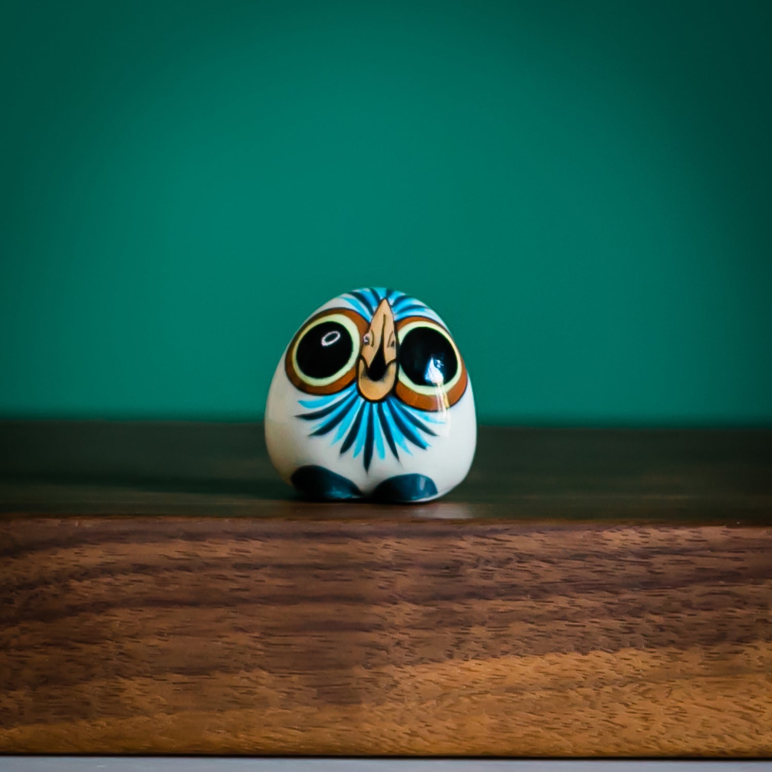 handpainted ceramic owl figurine with big eyes and blue feathers resting on wood block