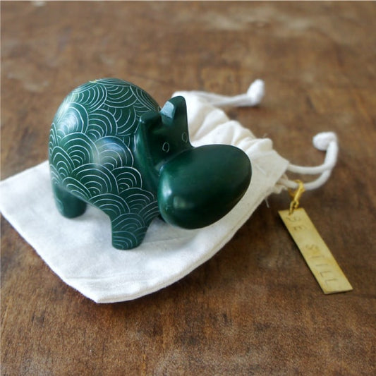 A hand-carved, green stone hippo with etched patterns, placed on a white cloth bag.