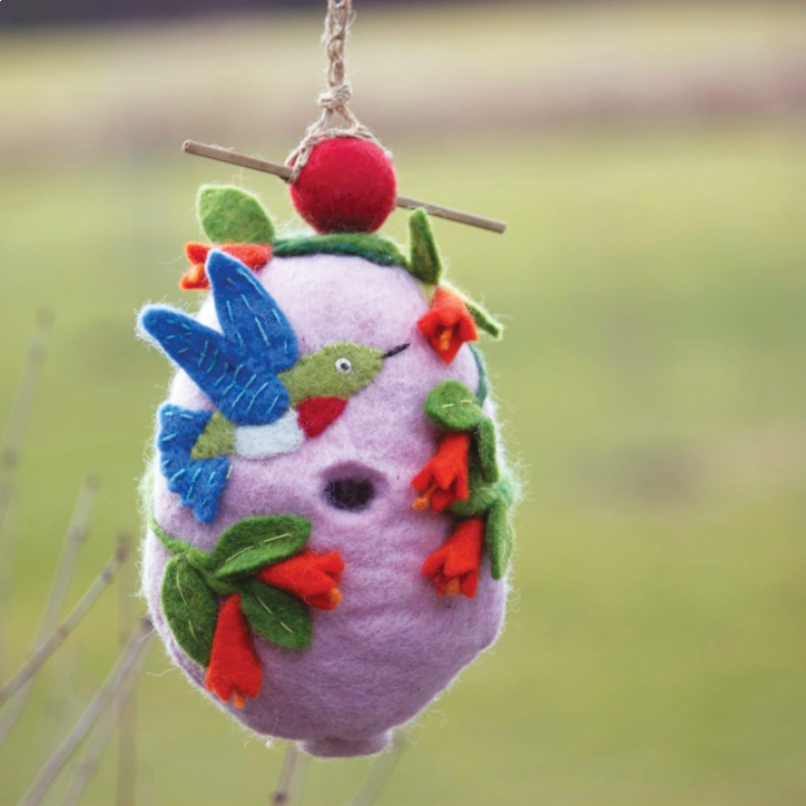 pink birdhouse with berries and a blue hummingbird on it in a field
